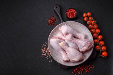 Taze çiğ tavuk bacağı, koyu beton arka planda tuz ve baharatlar.