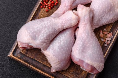 Taze çiğ tavuk bacağı, koyu beton arka planda tuz ve baharatlar.