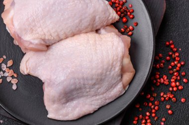 Taze çiğ tavuk butları, koyu beton arka planda tuz ve baharatlar.