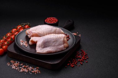 Taze çiğ tavuk butları, koyu beton arka planda tuz ve baharatlar.