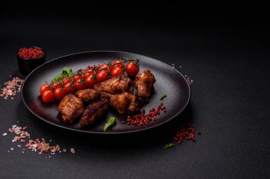 Izgarada pişirilmiş lezzetli sulu tavuk kanatları. Koyu beton arka planda tuz, baharat ve otlarla.