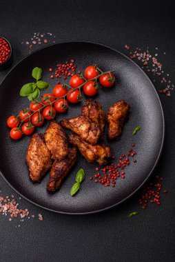 Izgarada pişirilmiş lezzetli sulu tavuk kanatları. Koyu beton arka planda tuz, baharat ve otlarla.