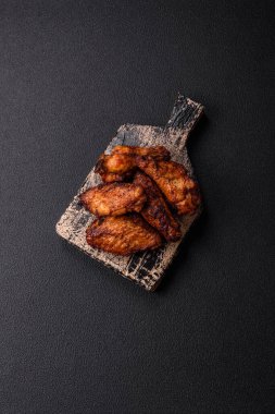 Izgarada pişirilmiş lezzetli sulu tavuk kanatları. Koyu beton arka planda tuz, baharat ve otlarla.