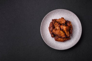 Izgarada pişirilmiş lezzetli sulu tavuk kanatları. Koyu beton arka planda tuz, baharat ve otlarla.