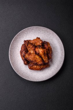 Izgarada pişirilmiş lezzetli sulu tavuk kanatları. Koyu beton arka planda tuz, baharat ve otlarla.