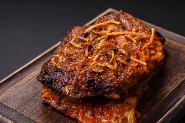 Delicious pork or beef ribs baked on the grill with salt, spices and herbs on a dark concrete background