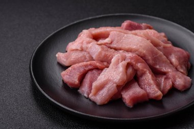 Koyu beton arka planda tuzlu, baharatlı ve otlu çiğ domuz eti veya hindi eti dilimleri