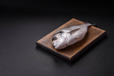 Limon, tuz, baharat ve otlu koyu beton arkaplanda çiğ dorado balığı.