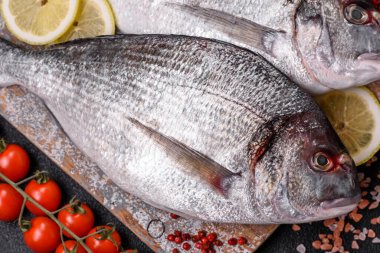 Limon, tuz, baharat ve otlu koyu beton arkaplanda çiğ dorado balığı.