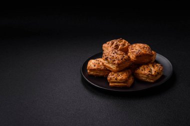 Feta peynirli üçgen puflar, esmer arka planda tuzlu domatesler, baharatlar ve otlar.