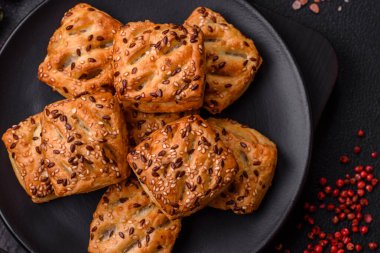 Feta peynirli üçgen puflar, esmer arka planda tuzlu domatesler, baharatlar ve otlar.