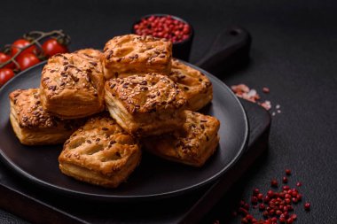 Feta peynirli üçgen puflar, esmer arka planda tuzlu domatesler, baharatlar ve otlar.