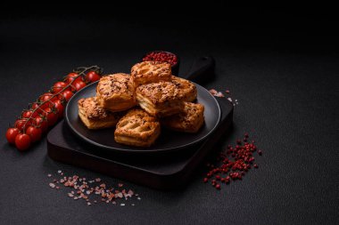 Feta peynirli üçgen puflar, esmer arka planda tuzlu domatesler, baharatlar ve otlar.