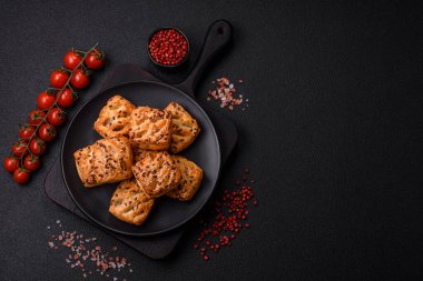 Feta peynirli üçgen puflar, esmer arka planda tuzlu domatesler, baharatlar ve otlar.