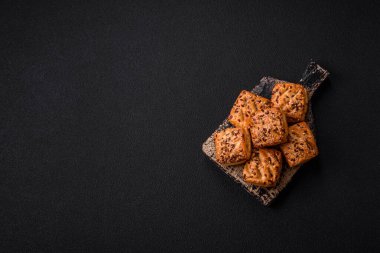 Feta peynirli üçgen puflar, esmer arka planda tuzlu domatesler, baharatlar ve otlar.