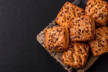 Feta peynirli üçgen puflar, esmer arka planda tuzlu domatesler, baharatlar ve otlar.