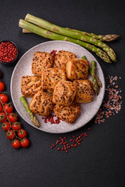 Feta peynirli üçgen puflar, esmer arka planda tuzlu domatesler, baharatlar ve otlar.