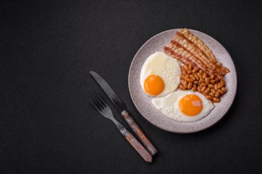 Yağda yumurta, pastırma, fasulye, domates, baharat ve bitkilerle İngiliz kahvaltısı. Güne doyurucu ve doyurucu bir başlangıç.