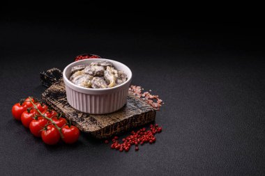 Kaynamış tavuk kalbi soğan ve krema sosuyla dilimlenmiş koyu beton arka planda tuz ve baharatla kesilmiş.