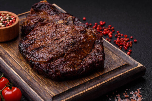 Delicious juicy beef ribeye steak grilled with salt, spices and herbs on a dark concrete background
