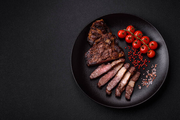 Delicious juicy beef ribeye steak grilled with salt, spices and herbs on a dark concrete background