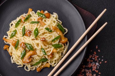 Lezzetli Asya mutfağı. İçinde pirinç, erişte, biber, mantar ve baharatlar var. Koyu beton arka planda.