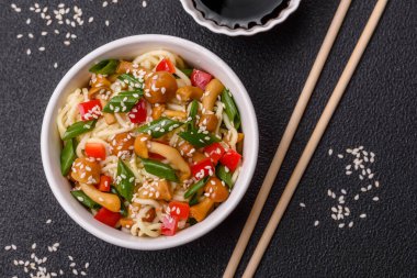 Lezzetli Asya mutfağı. İçinde pirinç, erişte, biber, mantar ve baharatlar var. Koyu beton arka planda.