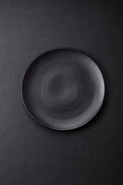 Empty ceramic round plate on dark textured concrete background. Cutlery, preparation for dinner