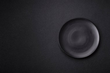 Empty ceramic round plate on dark textured concrete background. Cutlery, preparation for dinner