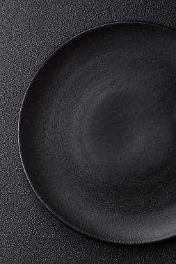 Empty ceramic round plate on dark textured concrete background. Cutlery, preparation for dinner