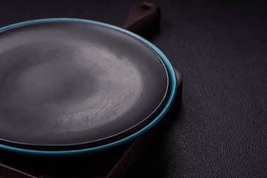 Empty ceramic round plate on dark textured concrete background. Cutlery, preparation for dinner