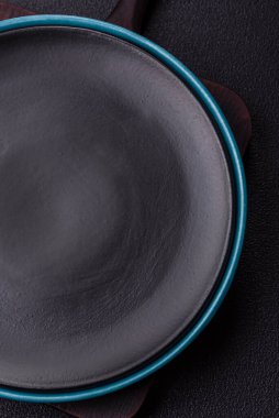 Empty ceramic round plate on dark textured concrete background. Cutlery, preparation for dinner