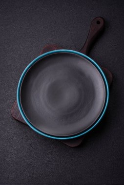 Empty ceramic round plate on dark textured concrete background. Cutlery, preparation for dinner