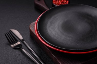 Empty ceramic round plate on dark textured concrete background. Cutlery, preparation for dinner
