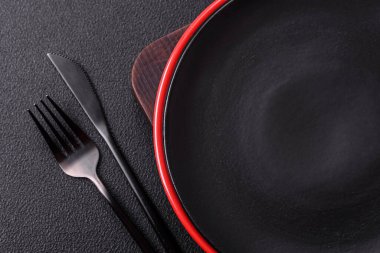 Empty ceramic round plate on dark textured concrete background. Cutlery, preparation for dinner