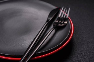 Empty ceramic round plate on dark textured concrete background. Cutlery, preparation for dinner