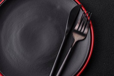 Empty ceramic round plate on dark textured concrete background. Cutlery, preparation for dinner