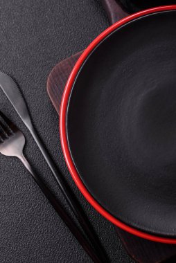Empty ceramic round plate on dark textured concrete background. Cutlery, preparation for dinner