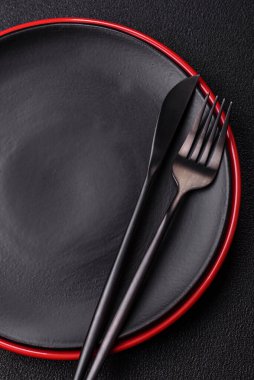 Empty ceramic round plate on dark textured concrete background. Cutlery, preparation for dinner