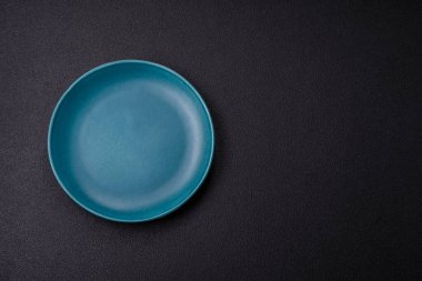 Empty ceramic round plate on dark textured concrete background. Cutlery, preparation for dinner