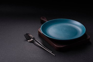 Empty ceramic round plate on dark textured concrete background. Cutlery, preparation for dinner