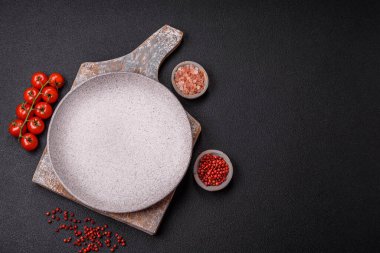 Empty ceramic round plate on dark textured concrete background. Cutlery, preparation for dinner