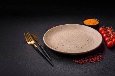 Empty ceramic round plate on dark textured concrete background. Cutlery, preparation for dinner