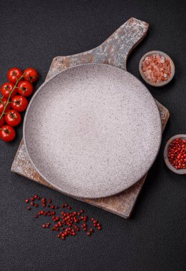 Empty ceramic round plate on dark textured concrete background. Cutlery, preparation for dinner