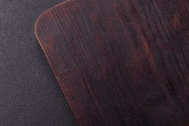 Boş ahşap kesme tahtası. Baharatlar, tuz ve otlar koyu beton arka planda.