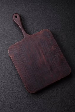 Boş ahşap kesme tahtası. Baharatlar, tuz ve otlar koyu beton arka planda.