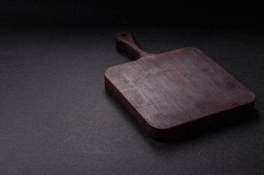 Boş ahşap kesme tahtası. Baharatlar, tuz ve otlar koyu beton arka planda.