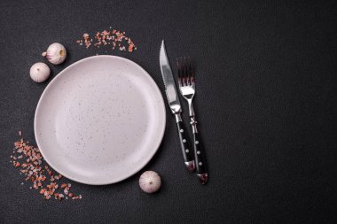 Empty ceramic round plate on dark textured concrete background. Cutlery, preparation for dinner