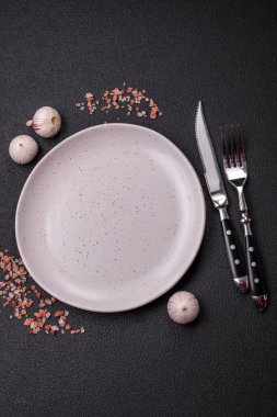 Empty ceramic round plate on dark textured concrete background. Cutlery, preparation for dinner