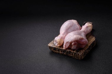 Tuzlu, baharatlı ve otlu çiğ tavuk budu. Koyu beton arka planda pişirmeye hazır.